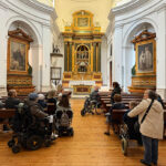 En la nave interior de la iglesia del monasterio donde se ubican las pinturas de Goya, el grupo de personas, algunas en silla de ruedas, atienden a la explicación.