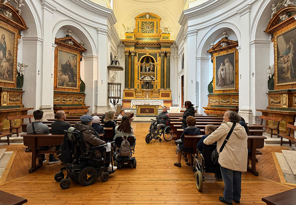 En la nave interior de la iglesia del monasterio donde se ubican las pinturas de Goya, el grupo de personas, algunas en silla de ruedas, atienden a la explicación.