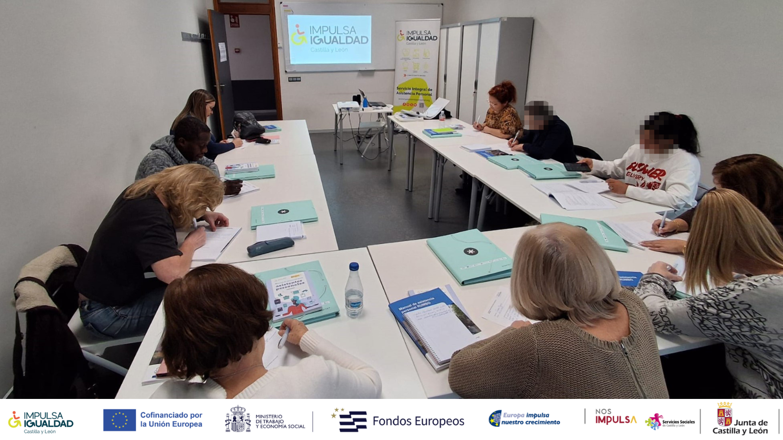 Participantes del proyecto escribiendo en el aula de las sesiones presenciales con el primer taller grupal de presentación. Abajo, logos organizadores y financiadores.