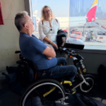 Un hombre en silla de ruedas con una mujer en una sala de espera de un aeropuerto.